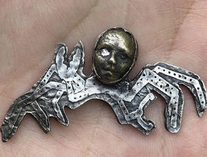 a hand holding a metal brooch with a face on it